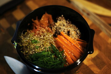 Homemade Korean Bibimbap bowl with fresh vegetables, sprouts, carrots, and sesame seeds on a wooden...