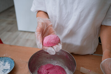 Person wearing transparent gloves shaping a round, pink mochi dough ball, carefully preparing this traditional japanese sweet dessert from a bowl of ingredients