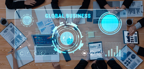 A group of professionals engaged in a modern business meeting around a table, showcasing digital analytics and financial data on various screens and devices. Trope