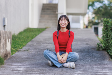 Fototapeta premium Happy asian student smiling sitting casually on campus path