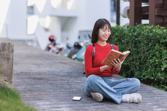 Young asian woman reading book outdoors smiling happily