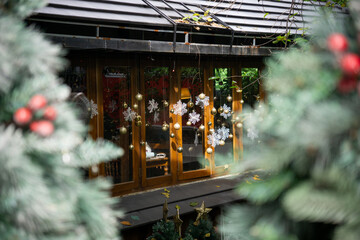 A festive window adorned with snowflake decorations and golden ornaments, framed by blurred Christmas greenery.