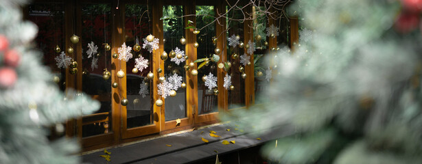Festive snowflake decals and golden ornaments adorn a glass door, framed by blurred Christmas greenery in the foreground