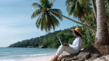 Woman is sitting on the beach with a laptop. She is wearing a straw hat. The beach is near a palm tree