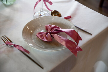 A beautifully set dining plate adorned with a pink satin ribbon, accompanied by elegant silverware on a crisp white tablecloth