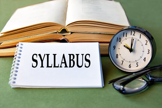 SYLLABUS text notebook with alarm clock, glasses and books on a green background