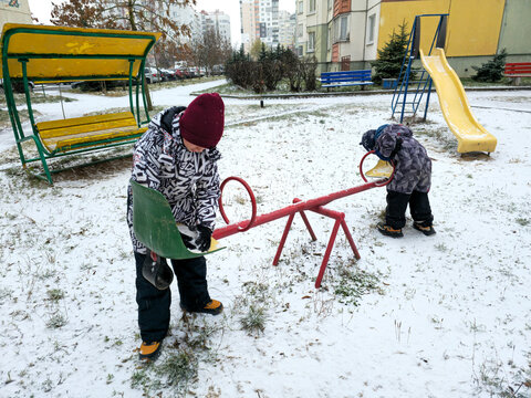 Two children playing on a slide in a playground during winter