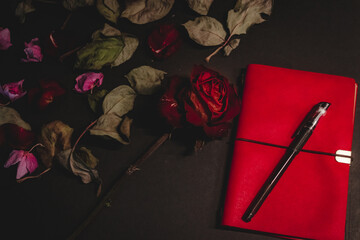 Dried red rose, notebook, pen symbolizing lost love