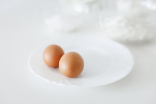 Two brown eggs resting on white plate, ready for baking