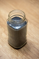 A glass jar filled with blue-gray poppy seeds on a wooden surface, shown from above, ideal for cooking, baking, nutrition, and long-term storage in airtight glass containers.