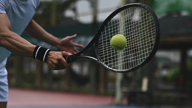 A tennis player swings the racket toward a fast-moving ball, captured in a dynamic close-up action shot on the court