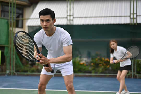 Front player crouches in a ready stance while the teammate stands behind, capturing a dynamic moment in tennis doubles training - Powered by Adobe