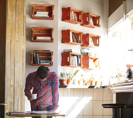 Man, reading and newspaper with coffee at house to start day, latest news and current events. Person, beverage and morning article for daily update, weather forecast and information of press coverage