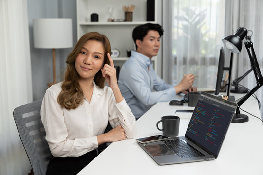 Profile smiling beautiful Asian businesswoman looking camera pose thinking creative project at modern office on working desk casual day. Blurry background man colleague analyzing data on pc. Infobahn.