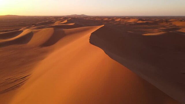 High altitude aerial drone shot gliding slowly over massive undulating desert dunes forming an infinite rhythm across a blank sandy landscape during golden hour undulating, infinite, aerial