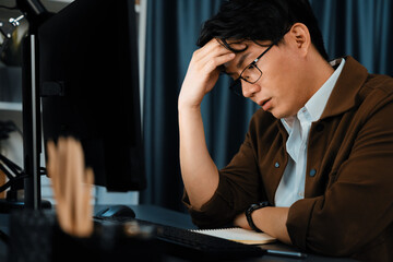 Smart businessman with stressful face working on pc to create business plan report over late night...