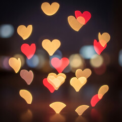 Heart-shaped bokeh lights in warm red and yellow hues creating a romantic and dreamy atmosphere against a dark, blurred background.