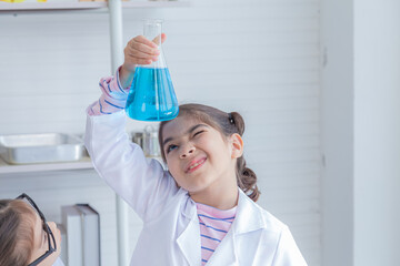 Cheerful Arabian student girl wearing eyeglasses using magnifier glass looking smoke liquid experiment in flask, pupil kid in lab coat uniform having fun attention to cylinder test, a future scientist