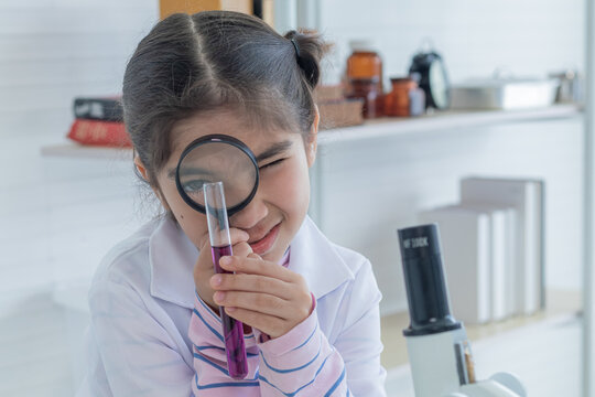 Cute Arabian girl elementary student kid wearing lab coat standing near microscope hold glass magnifier looking at camera in laboratory classroom, lifestyle learning education science class scientist - Powered by Adobe