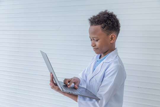 Cheerful African American boy elementary student kid hold technology laptop for studying in science class, cute primary school pupils happy typing keyboard wearing lab coat uniform, education concept
