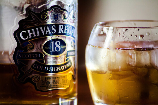 Slavsk / Ukraine - 07.22.2019: Bottle of Chivas Regal 18yr Gold Signature Blended Scotch Whisky & glass with a logo of this whiskey on a dark background, on a wooden table, horizontal, no one, closeup