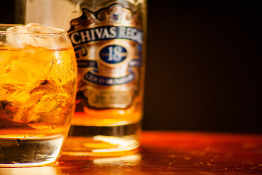 Slavsk / Ukraine - 07.22.2019: Bottle of Chivas Regal 18yr Gold Signature Blended Scotch Whisky & glass with a logo of this whiskey on a dark background, on a wooden table, horizontal, no one, closeup