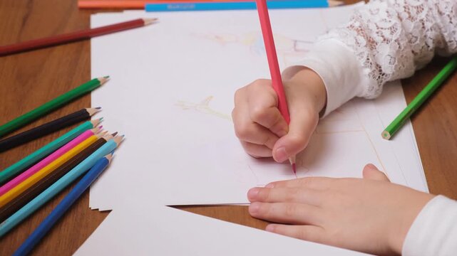 Young kid creating simple drawing with pink pencil on large sheet, pile of multicolored pencils nearby, imaginative playtime for art therapy, kids workshops and creative lifestyle content