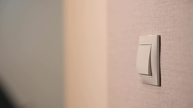 Close-up of a hand pressing a wall light switch indoors, illustrating electricity control, energy saving and everyday household actions in a modern home interior.
