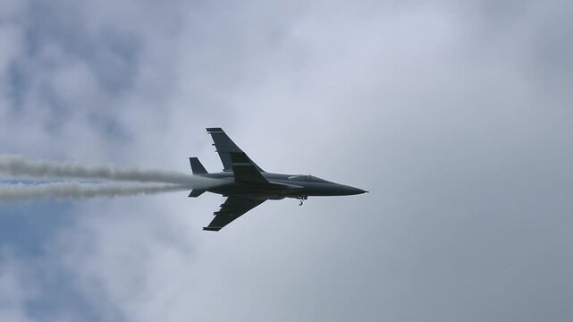 Dark Jet Aircraft in Cloudy Sky with Smoke and Visible Jet Wash During Flight