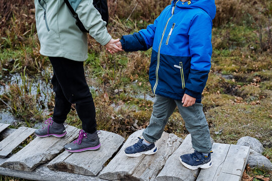siblings exploring nature together, two young explorers with colorful clothing on woodland pathway, brothers and sisters carefully traverse mossy boardwalk amid puddles and fall scenery