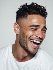Obraz premium Young man laughing aloud with eyes closed and mouth wide open on a plain background. Happy natural emotion and authentic human expression.