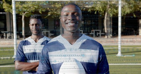 Smiling male athlete holding white football on grassy field, wearing navy and white jerseys