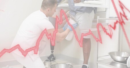 Kneeling clinician adjusting prosthetic leg in clinic room in white scrubs and blue gloves
