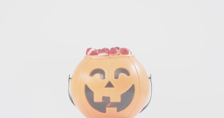 Displaying orange jack-o'-lantern bucket sitting on white tabletop, showing candies and molded face