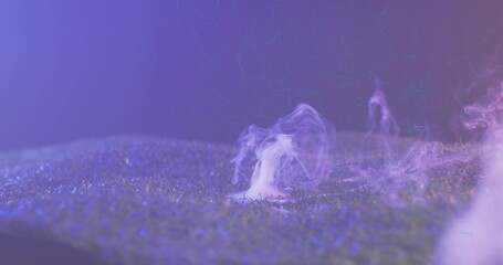 Rising single white smoke plume drifting over turf with dew under purple-blue lights in studio set