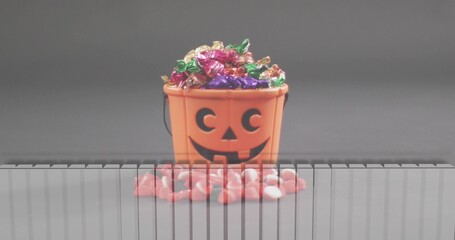Showing orange pumpkin bucket holding foil and pink white candies on gray tabletop, striped panel © vectorfusionart