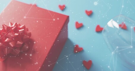 Red gift box sitting on blue tabletop, showing heart confetti, tilted stemmed glass, dotted overlay