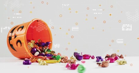 Tipping orange jack-o-lantern pail spilling foil candies and heart candy on white table, copy space