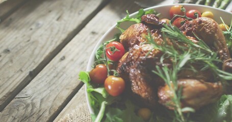 Showing roasted chicken in white bowl on rustic table with greens rosemary cherry tomatoes on vine