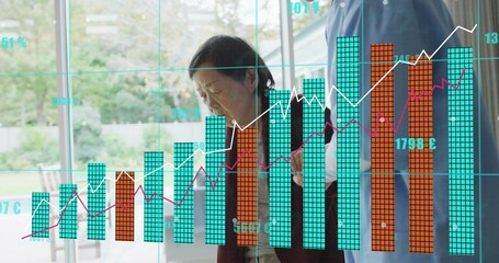 Standing carer blue top helping senior cardigan behind glass at home, holding phone, chart overlay