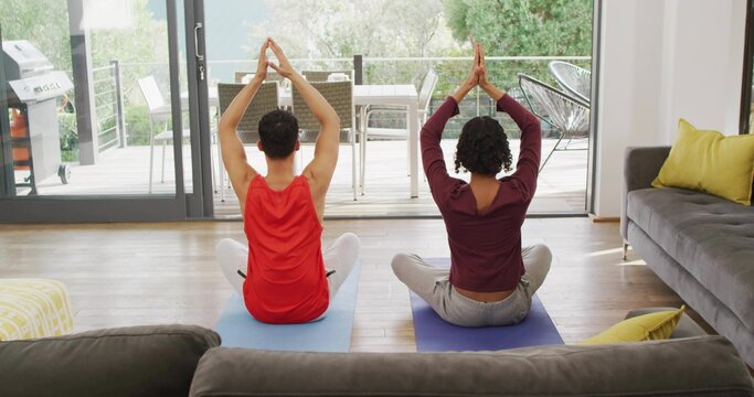 Stretching two adults raising arms overhead on yoga mats in living room, wearing workout tops