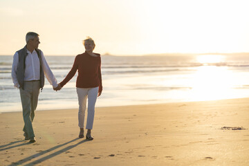 Senior couple walking beach holding hands enjoying sunset