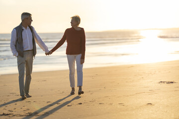 Senior couple walking hand in hand along beach at sunset