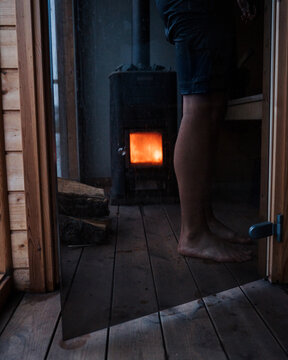 mans feet stood next to a log fire floating sauna in Sweden