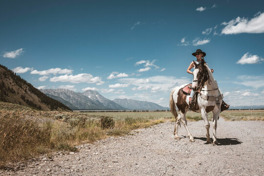 Young cowgirl wrangles her horse along dirt road in Jackson, Wyoming