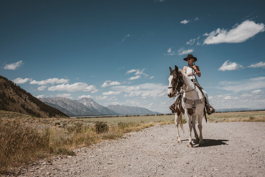 beautiful young woman and horse riding along gravel road in Wyoming
