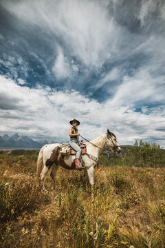 Female in tank top hold reigns of her horse on ranch, Jackson Hole