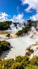 Steaming thermal pools reflect the sky, surrounded by lush foliage on a sunny day with scattered white clouds