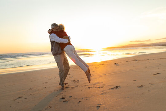Senior couple embracing, having fun playing on beach at sunset - Powered by Adobe