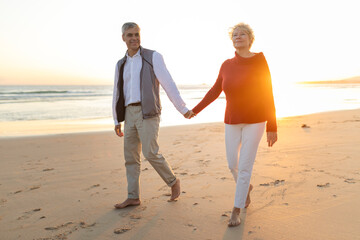 Senior couple enjoying romantic beach walk holding hands